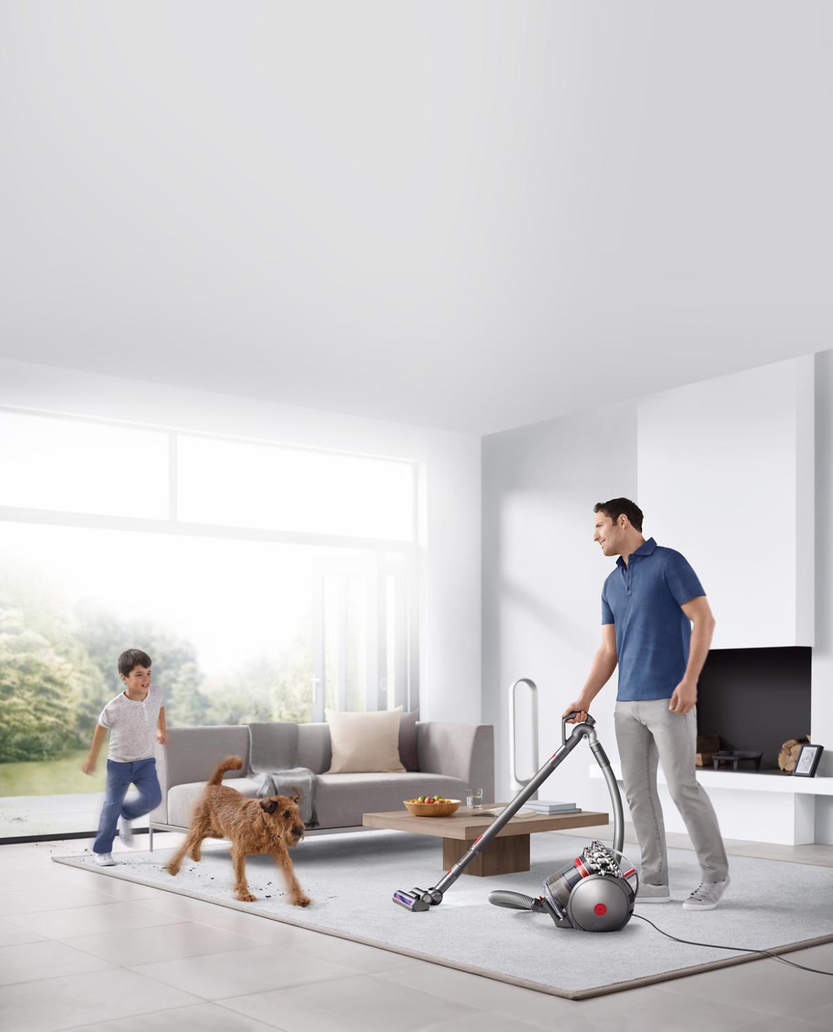 Man vacuuming in room with dog and child