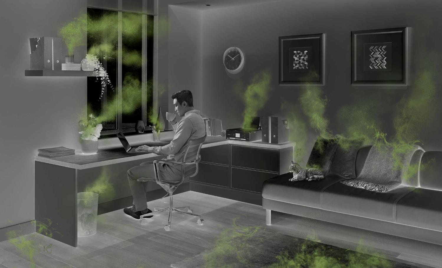 Man working at home office desk with sources of air pollution coming from objects around the room.
