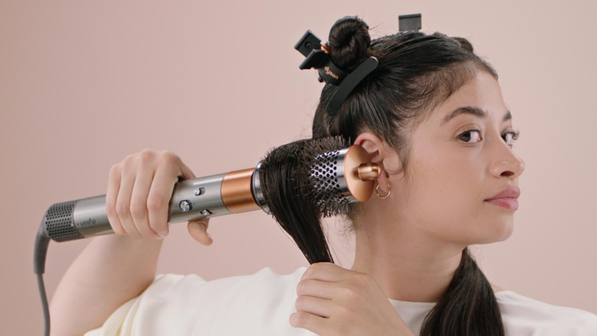 A model styling her hair with the Dyson Airwrap multi-styler and Large round volumising brush.