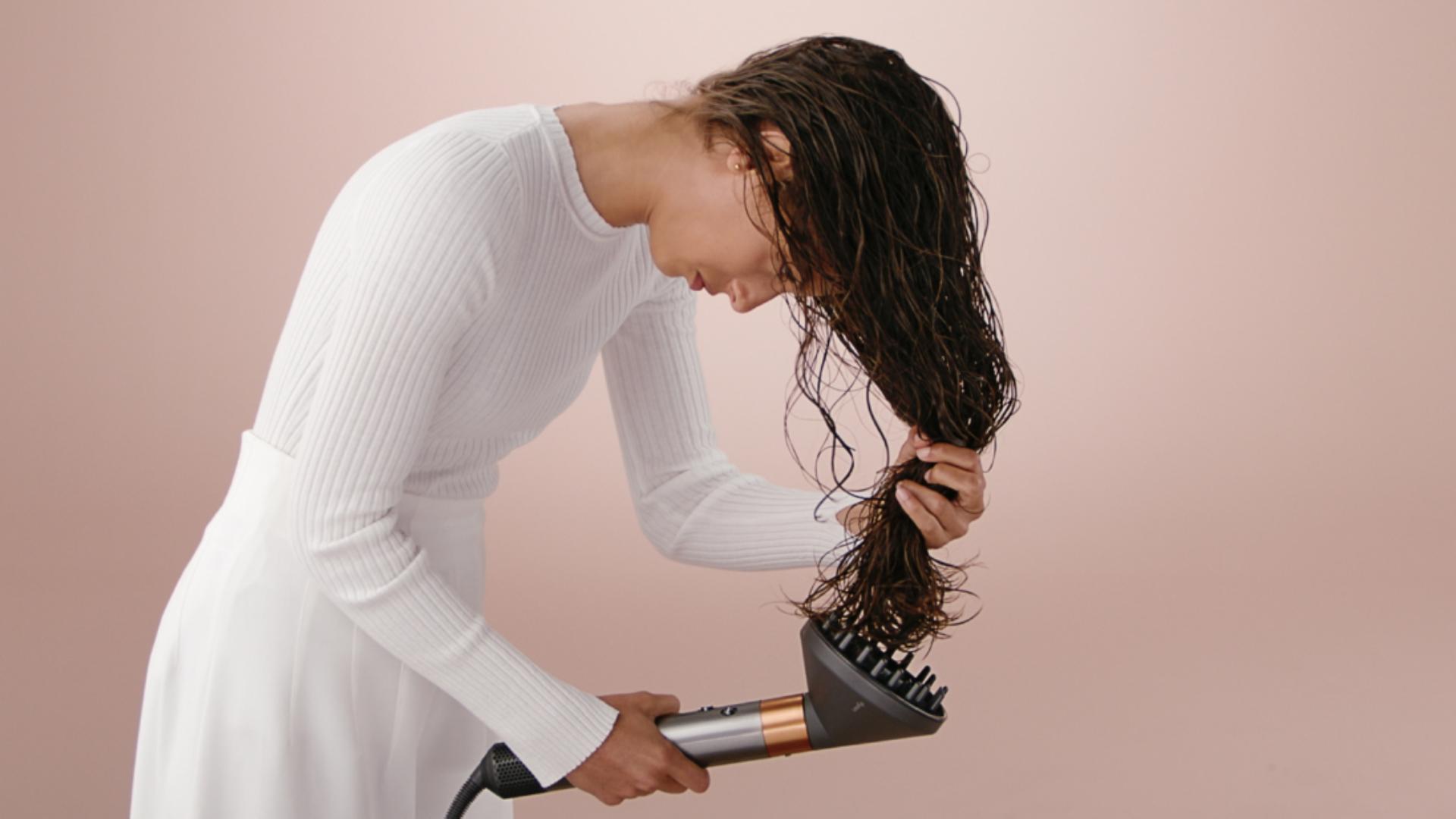 A model styling her hair with the Dyson Airwrap multi-styler and Diffuser attachment.