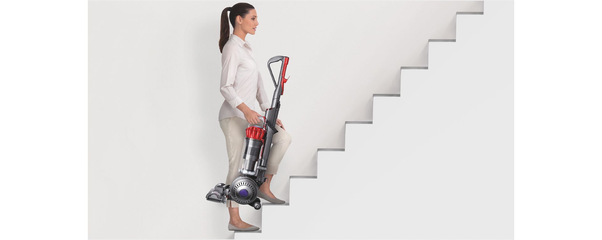Woman carrying an upright vacuum up a set of stairs.