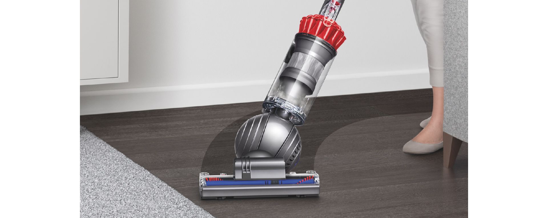 Upright vacuum cleaner being steered in a sweeping arc across a black hard floor surface. 