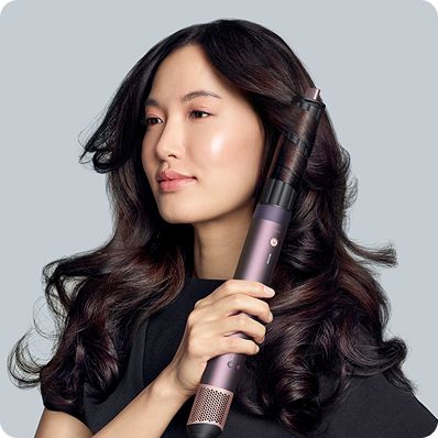 A model with dark hair adds curls using the Dyson Airwrap Co-anda2x multi-styler and dryer.