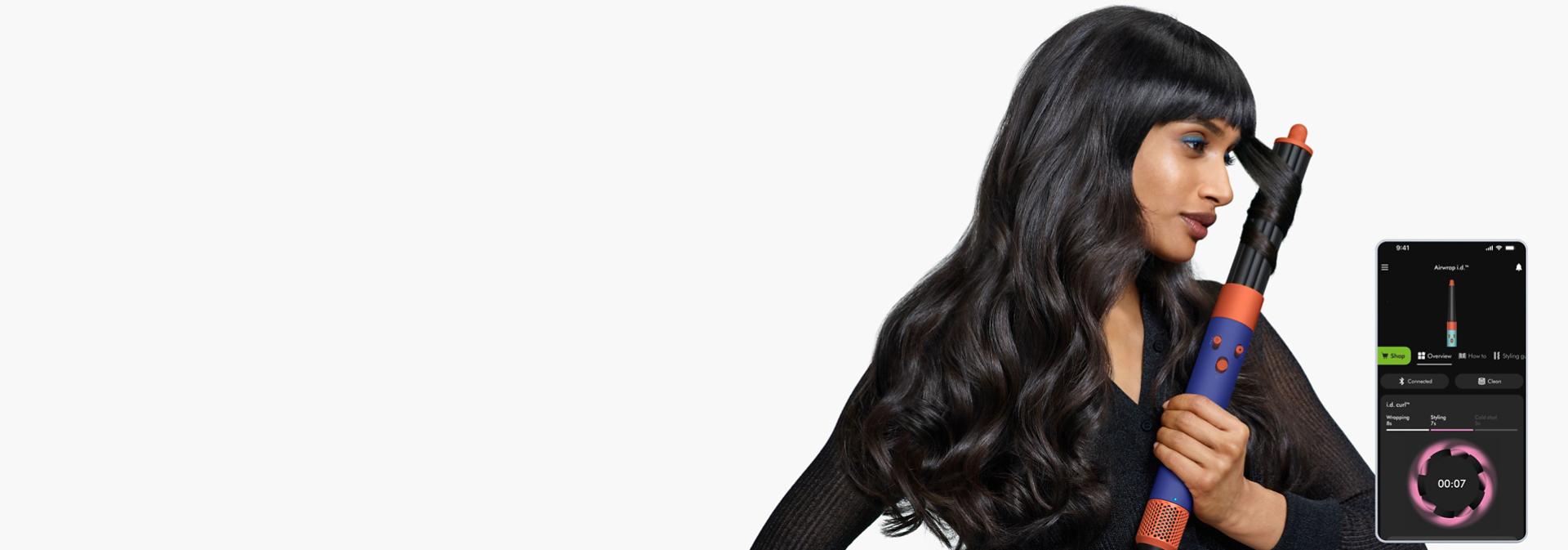 Multistyler Dyson Airwrap i.d. używany przez modelekę, z ekranem smartfona obok, pokazującym aplikację MyDyson.