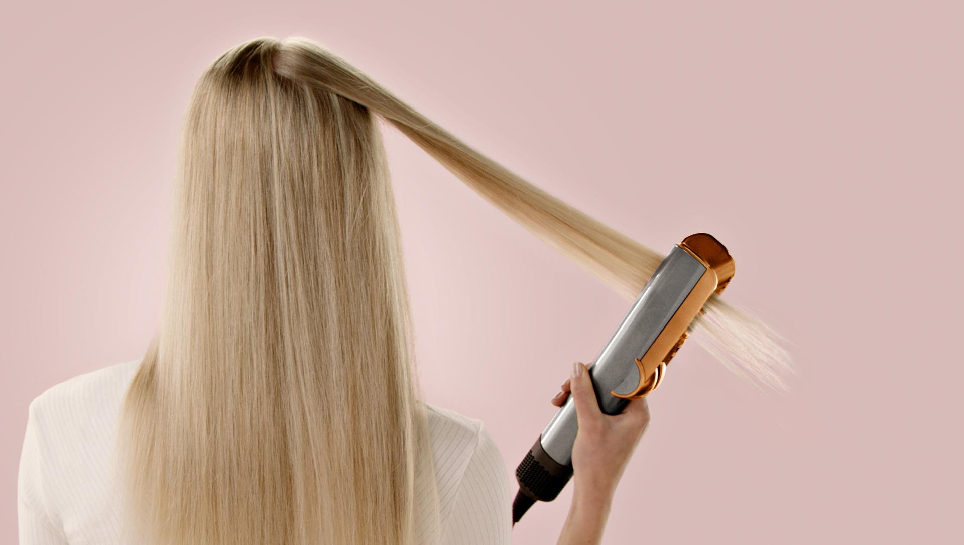 A model uses a Dyson Airstrait to straighten a tress of hair.