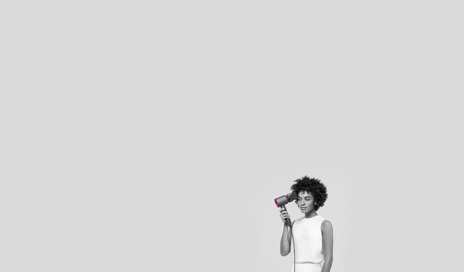 Une femme utilisant le Dyson Supersonic avec l’accessoire à dents larges