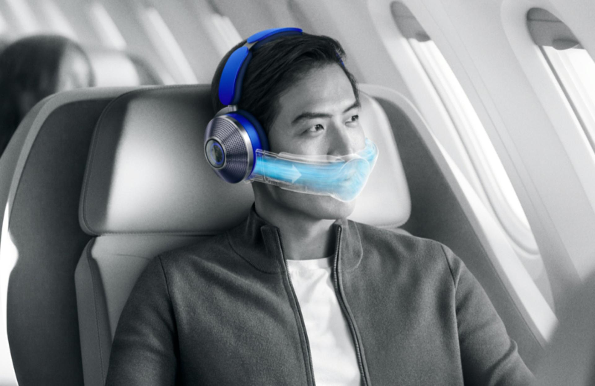 Uçakta otururken hava temizleme özellikli Dyson Zone kulaklık kullanan bir adam.