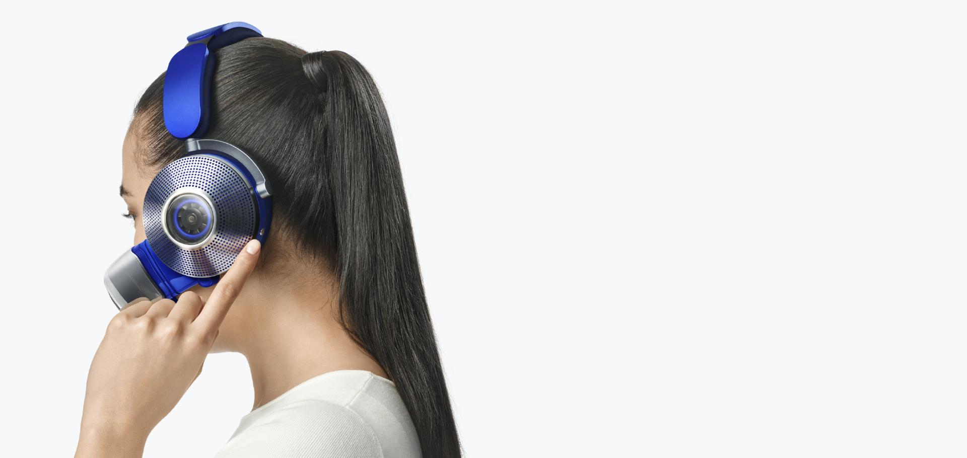Woman taps the side of the ear cup to change modes on the Dyson Zone air-purifying headphones.