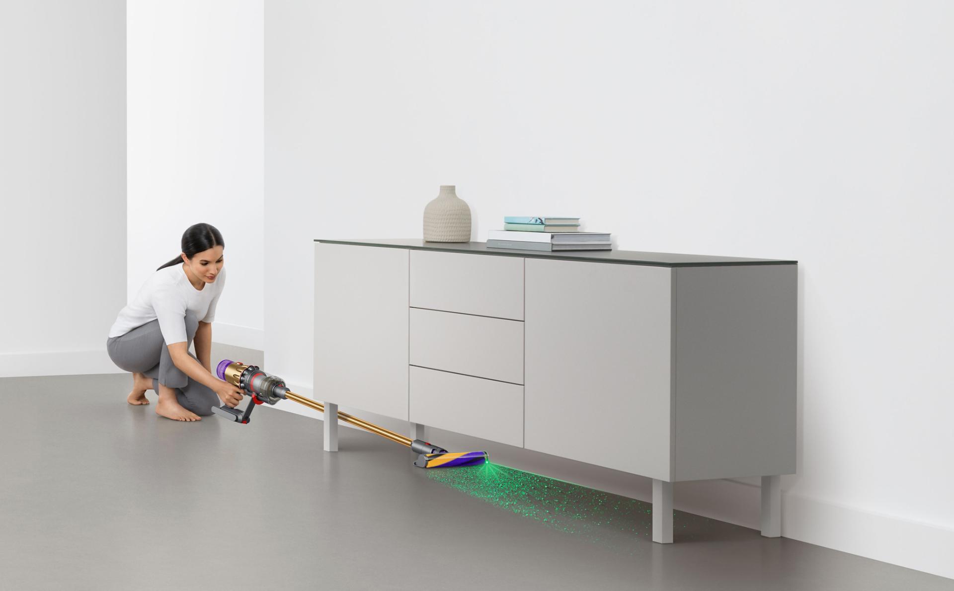 سيدة تستخدم مكنسة Dyson V12 Detect Slim للتنظيف تحت خزانة.