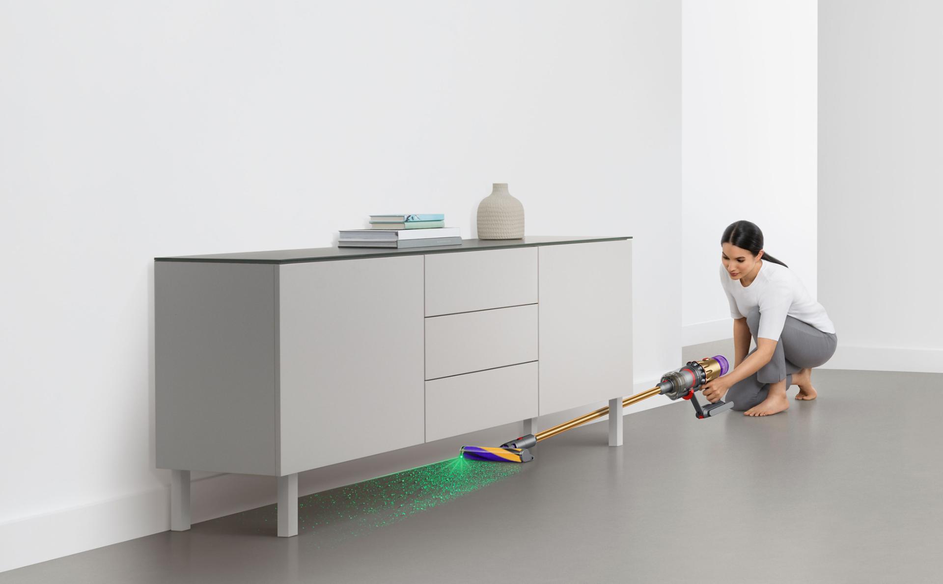 Dyson V15 Detect vacuum vacuuming under a grey sofa.