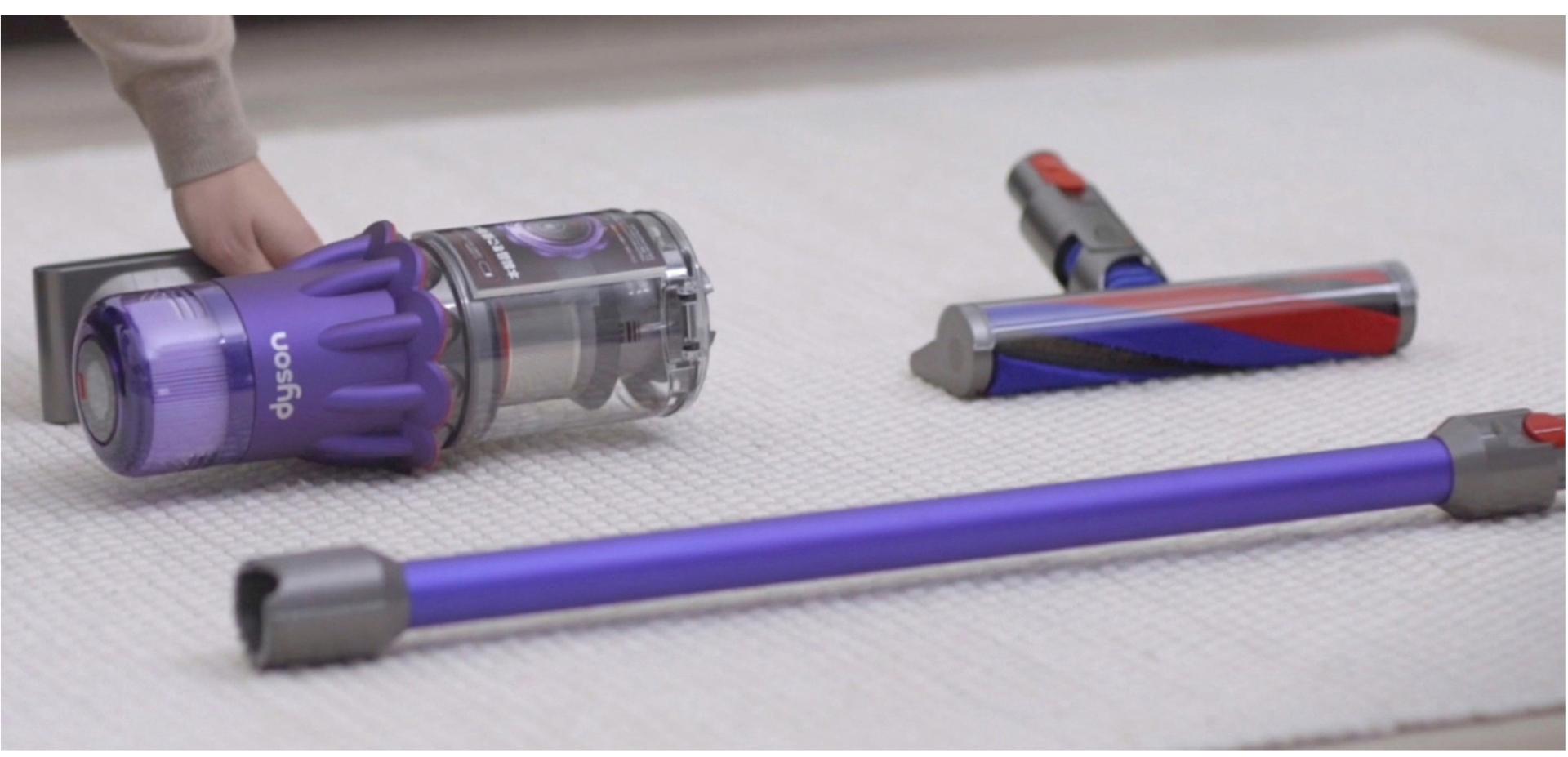 Dyson Digital Slim vacuum resting on the floor with a hand picking it up.