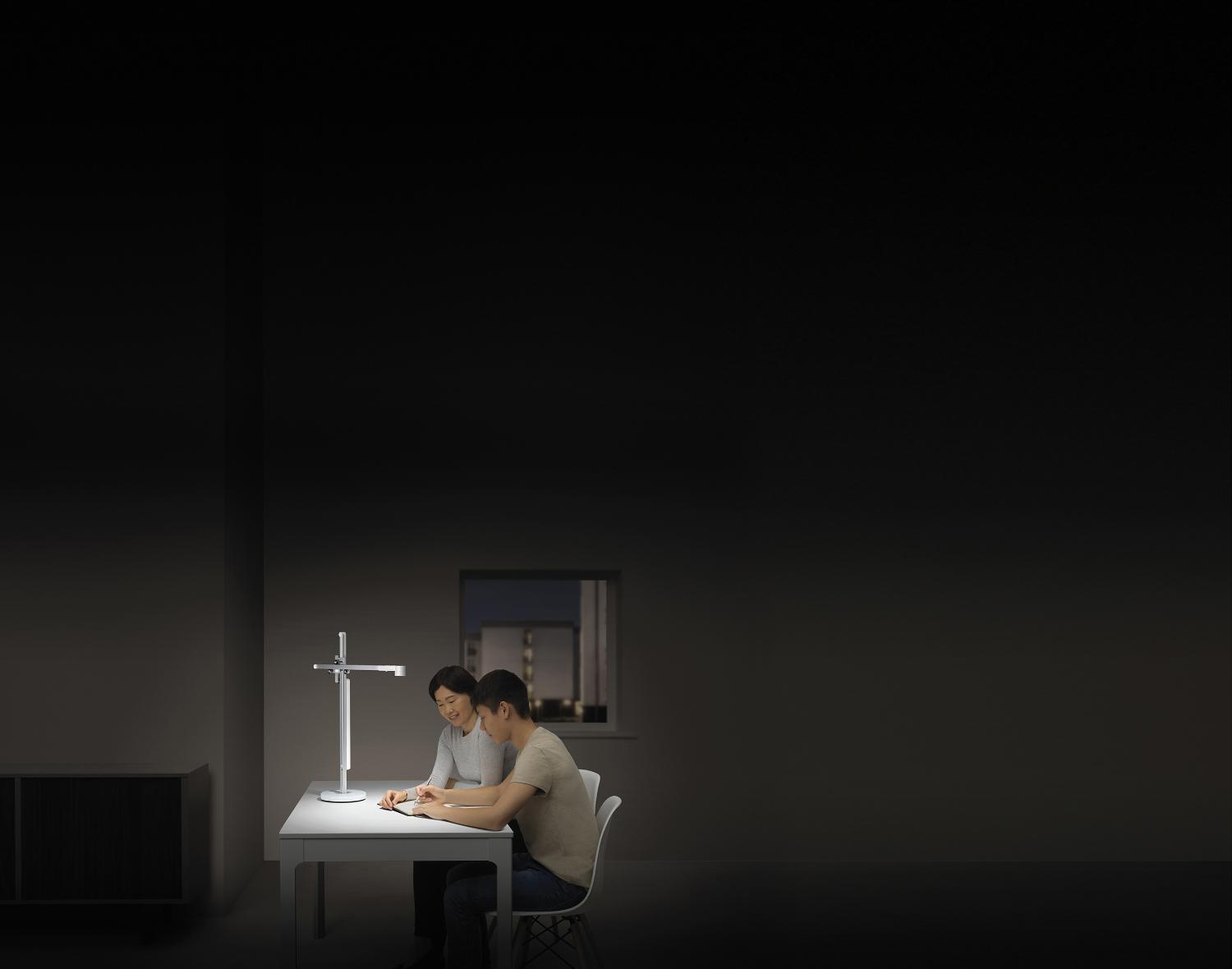 Teenager studies with his mother in powerful desk light