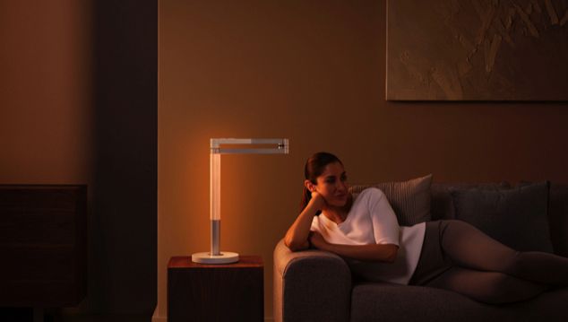 Женщина расслабляется под элегантным оранжевым светом, излучаемым Dyson Lightcycle Morph, в позиции для создания настроения