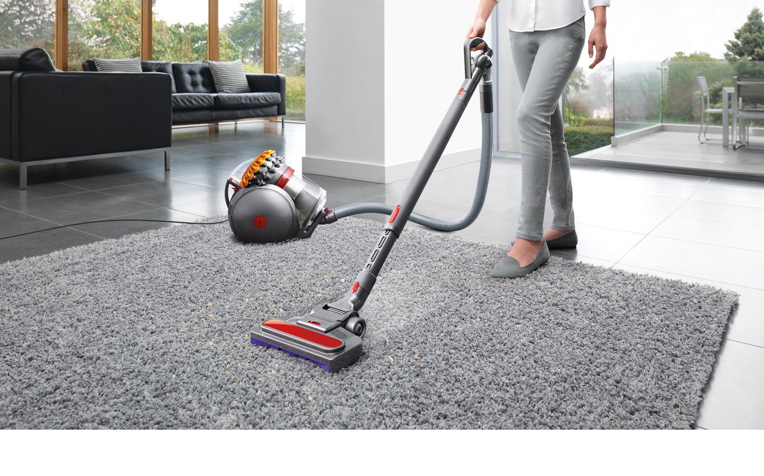 Model dat een Dyson Big Ball gebruikt voor het reinigen van een grijs tapijt in een woonkamer.