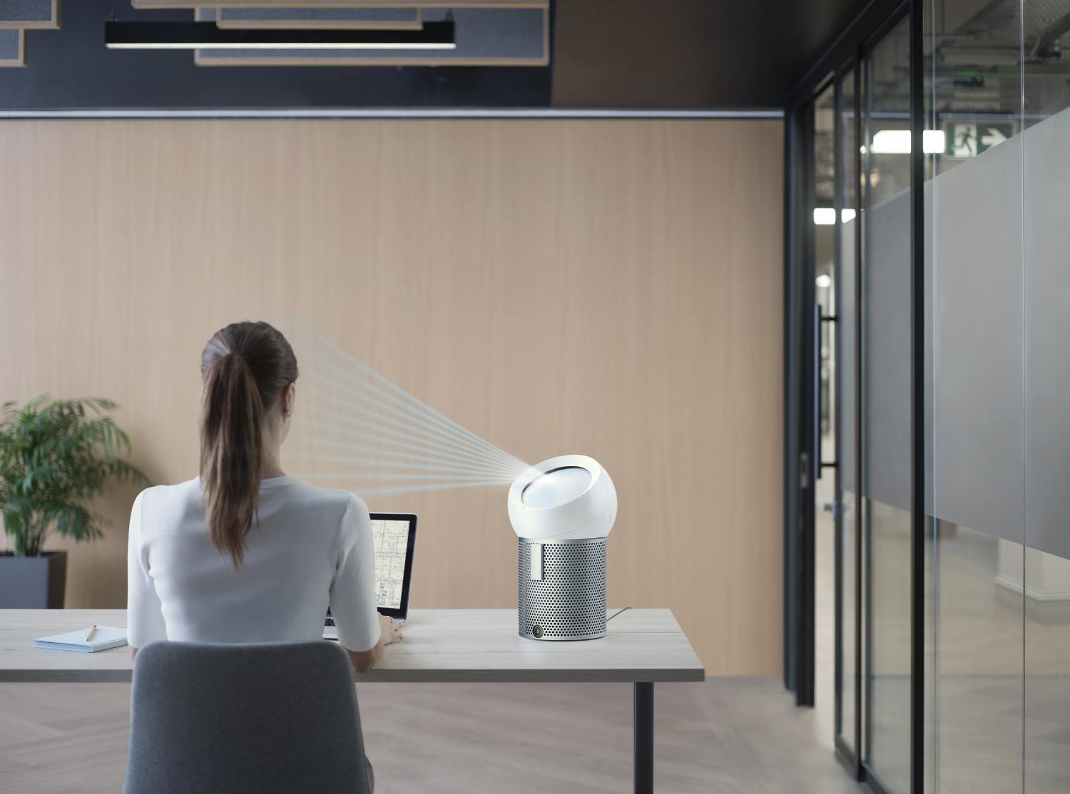 Woman working at a desk with the Dyson Pure Cool Me personal purifying fan projecting purified air