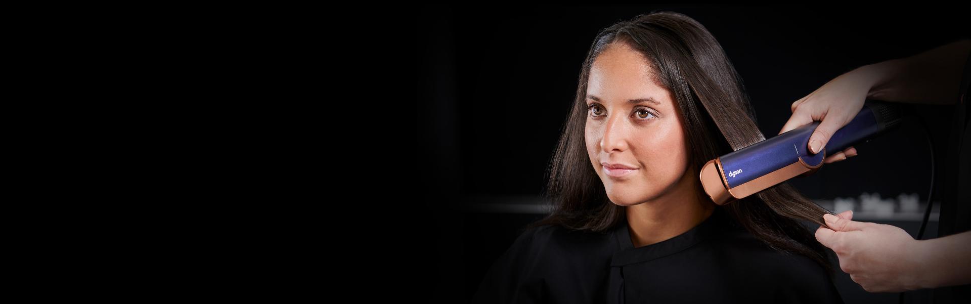 Włosy kobiety są profesjonalnie stylizowane poprzez prostownicę Dyson Airstrait.