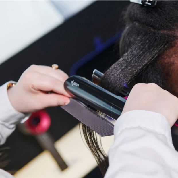 Bir kadının saçını şekillendirmek için Dyson Airstrait kullanan bir saç stilisti