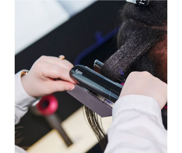 Bir kadının saçını şekillendirmek için Dyson Airstrait kullanan bir saç stilisti