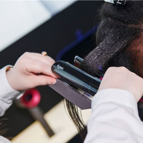A hairstylist using a Dyson Airstrait to style a woman's hair 