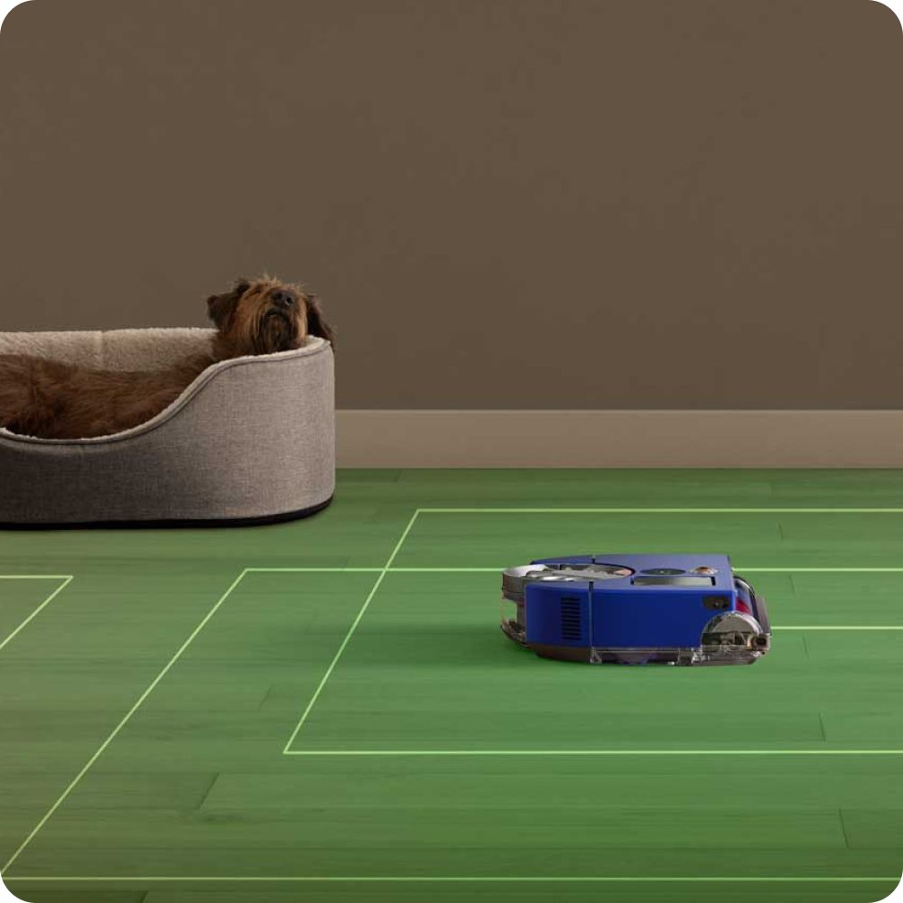 A Dyson robot vacuum cleaner navigating a room while a dog rests in a bed nearby.