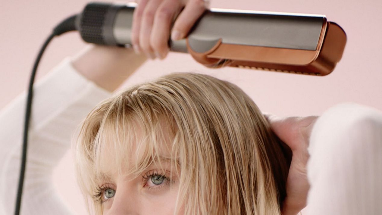 The Dyson Airstrait straightener is used to pre-dry the roots of a model’s hair before styling. The Dyson Airstrait straightener is used to pre-dry the roots of a model’s hair before styling.