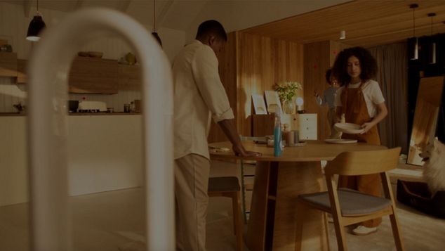 A man sprays cleaning product in a modern, open plan kitchen and living space just before meal time