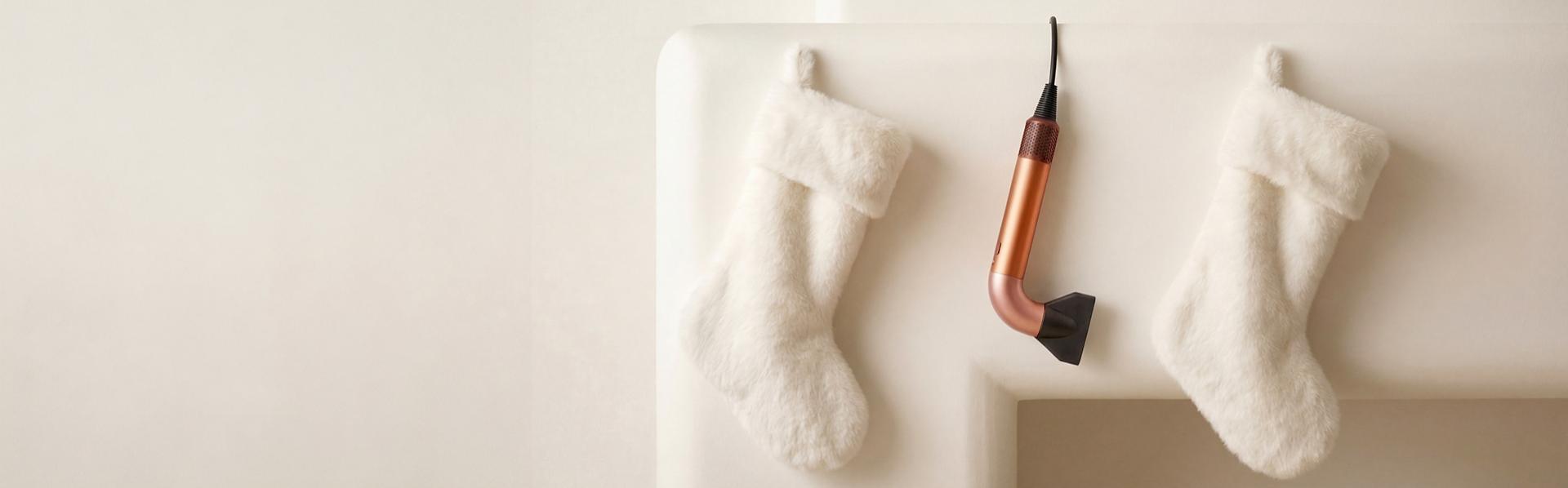 The Dyson Supersonic r hair dryer hanging in a line between a pair of Christmas stockings.