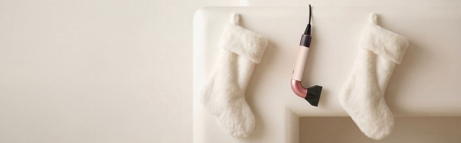 The Dyson Supersonic r hair dryer hanging in a line between a pair of Christmas stockings.