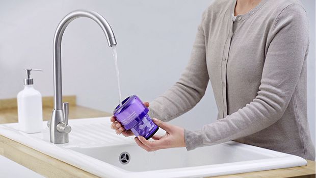 A Dyson filter is cleaned under running water from a tap.