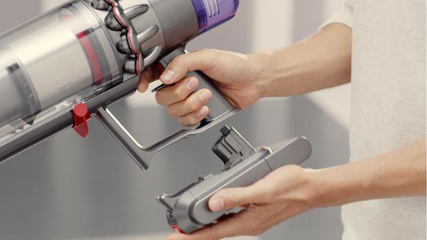 A battery is clicked into place on the handle of a Dyson vacuum.