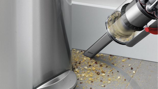 The crevice tool cleans crumbs from a nook next to a bin.
