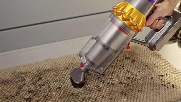 A Dyson vacuum is used with the Stubborn dirt brush to deep-clean a welcome mat in a home.
