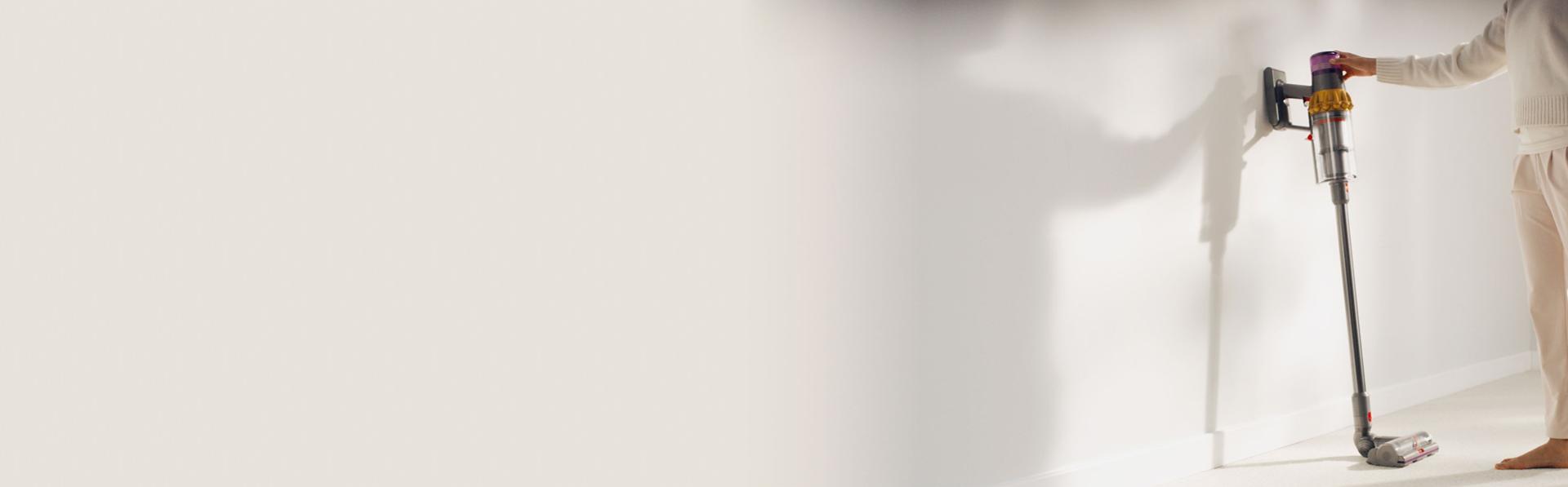 A person cleans underneath a low cabinet with a Dyson vacuum and the Low-reach adaptor.