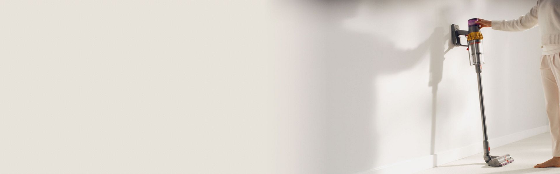 A person cleans underneath a low cabinet with a Dyson vacuum and the Low-reach adaptor.