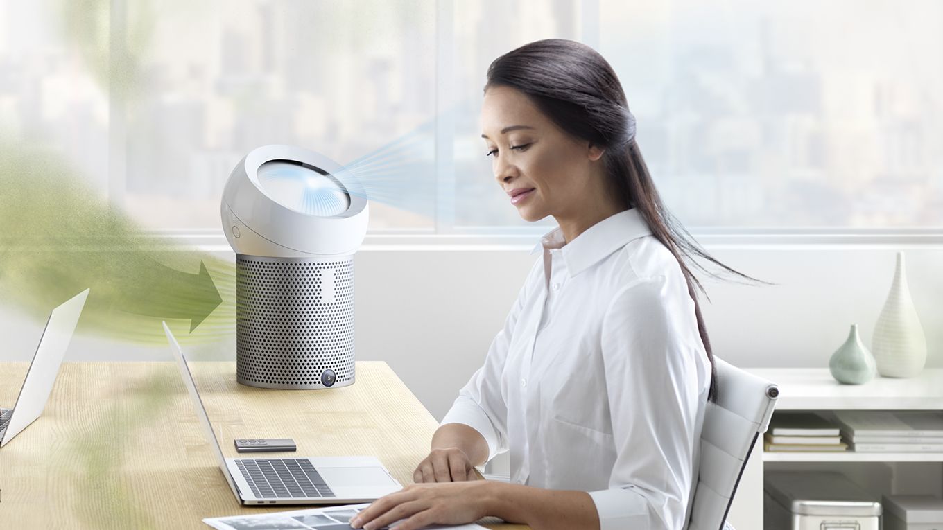A woman working at her desk in her home using a Pure Cool Me purifying fan