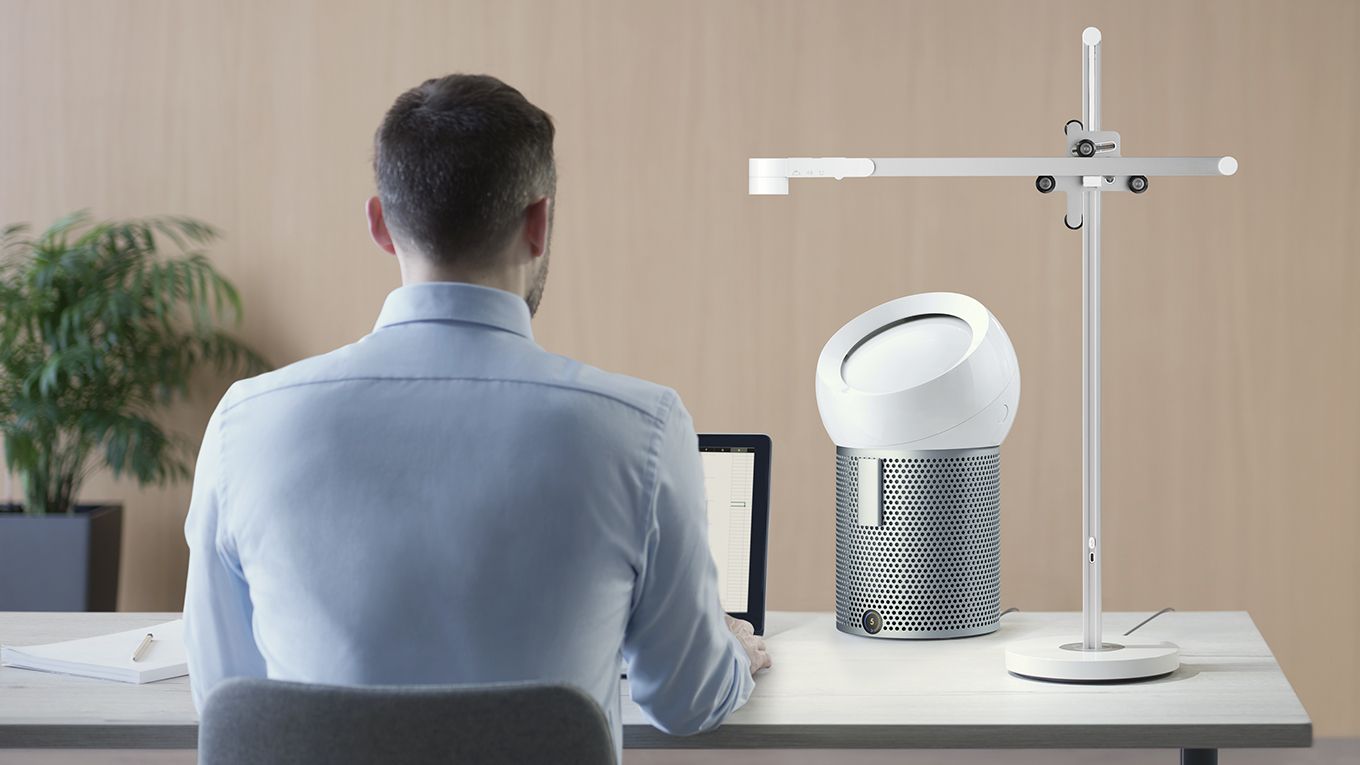 A man working from home using a Dyson Lightcycle Task Light and and a Pure Coole Me purifying fan