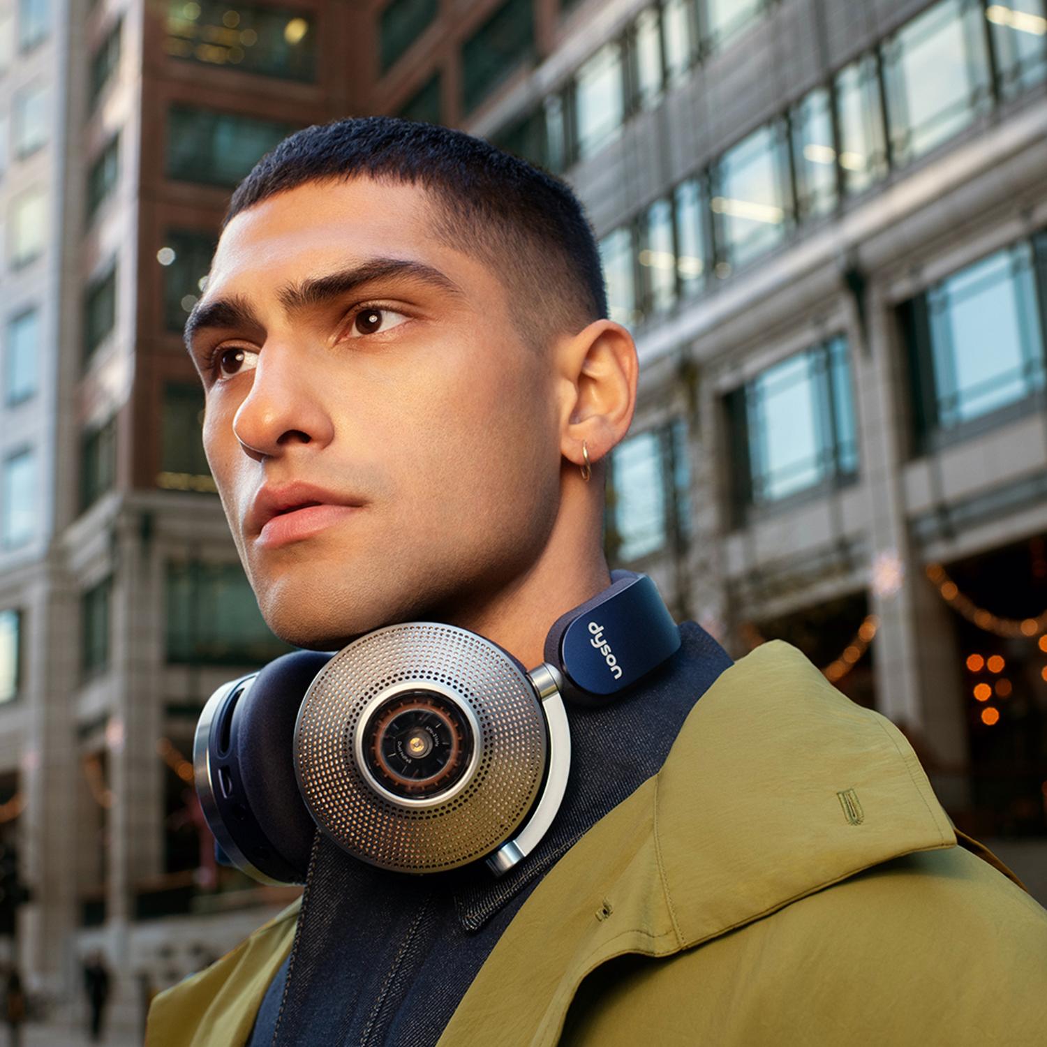 A man stands in an urban street with the Dyson Zone noise-cancelling headphones resting around his neck.