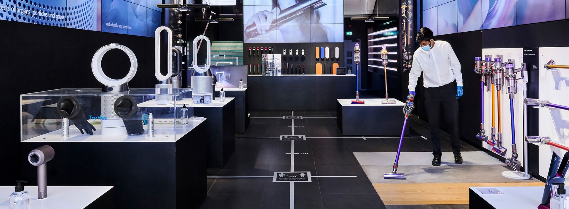 Dyson expert in mask using Dyson cordless vacuum to clean Dyson Demo store. 