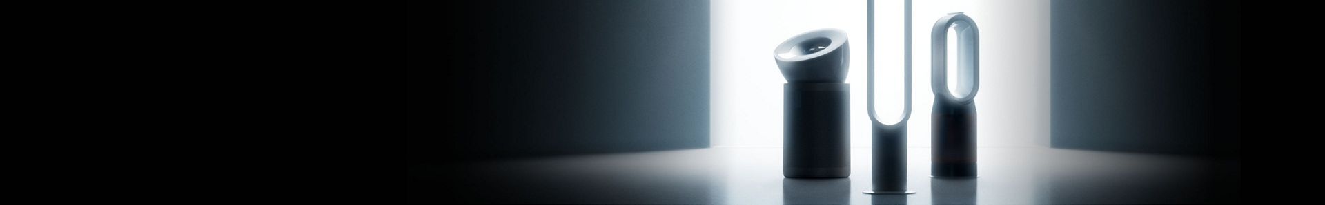 A lineup of sleek Dyson appliances, including air purifiers, heaters and more arranged in a dark room.