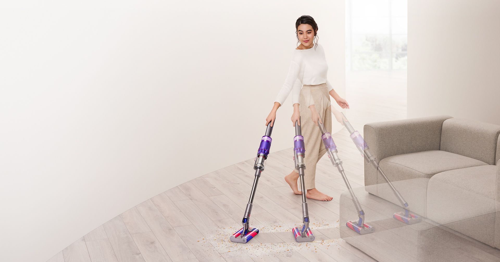 En kvinde støvsuger hårde gulve og rundt om en sofa med Dyson Omni-glide™-støvsugeren.