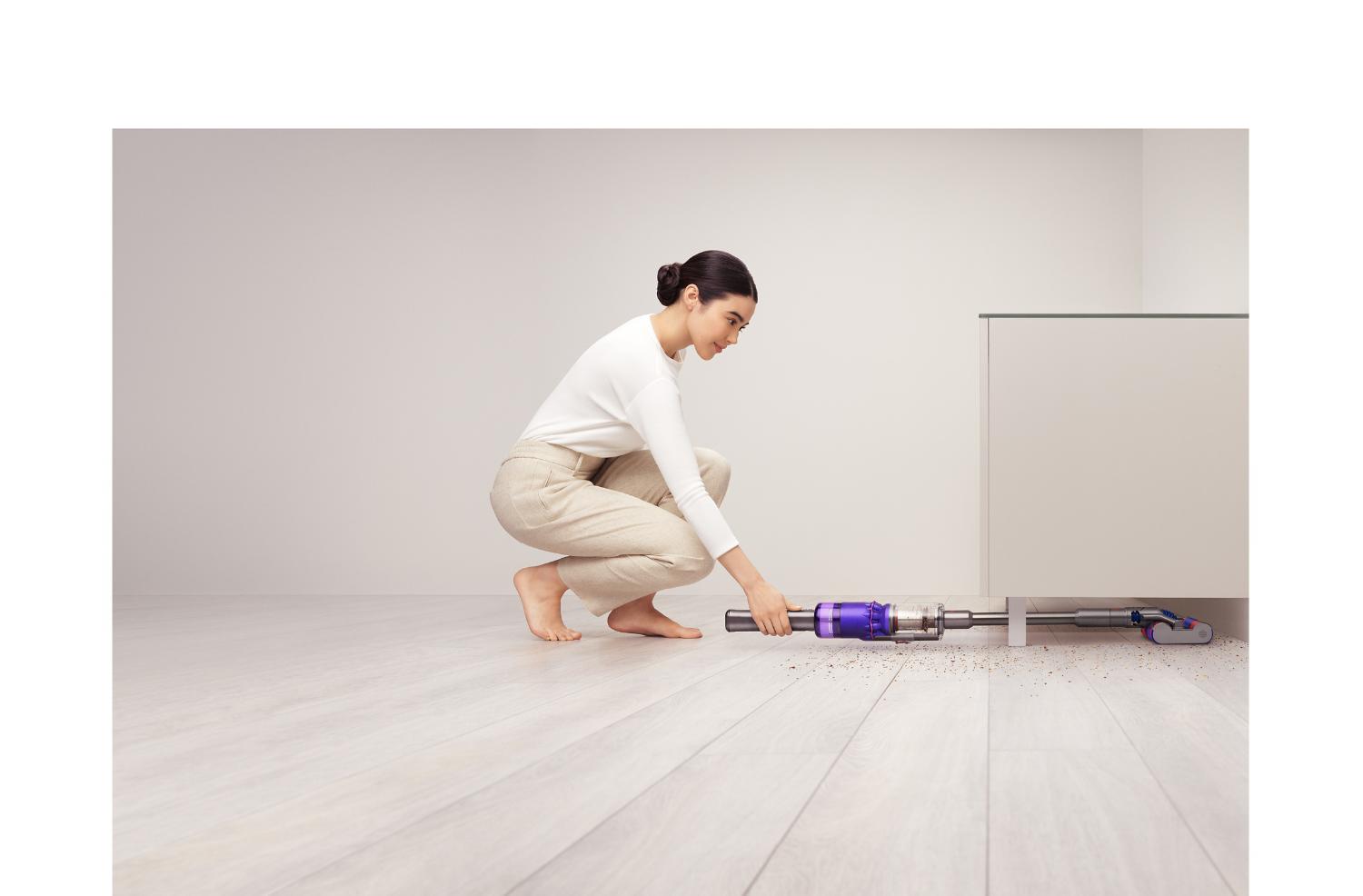 Frau verwendet den Dyson Omni-glide™ Staubsauger, um unter einem Schrank zu reinigen.