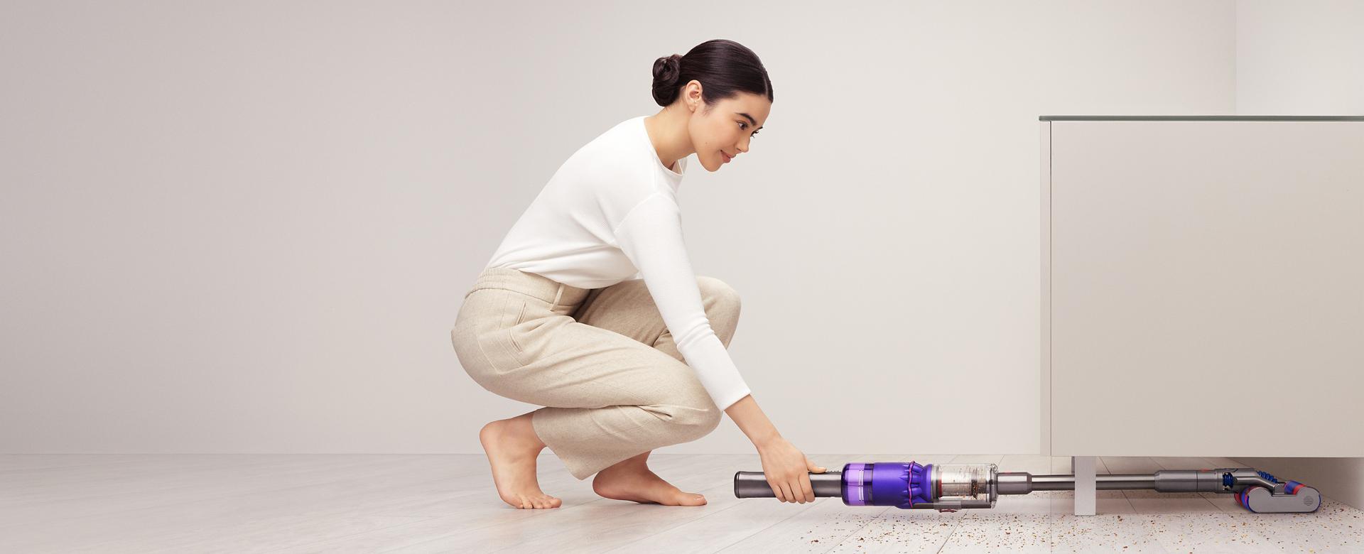 女子使用 Dyson Omni-glide™吸塵機清理碗櫥下方。