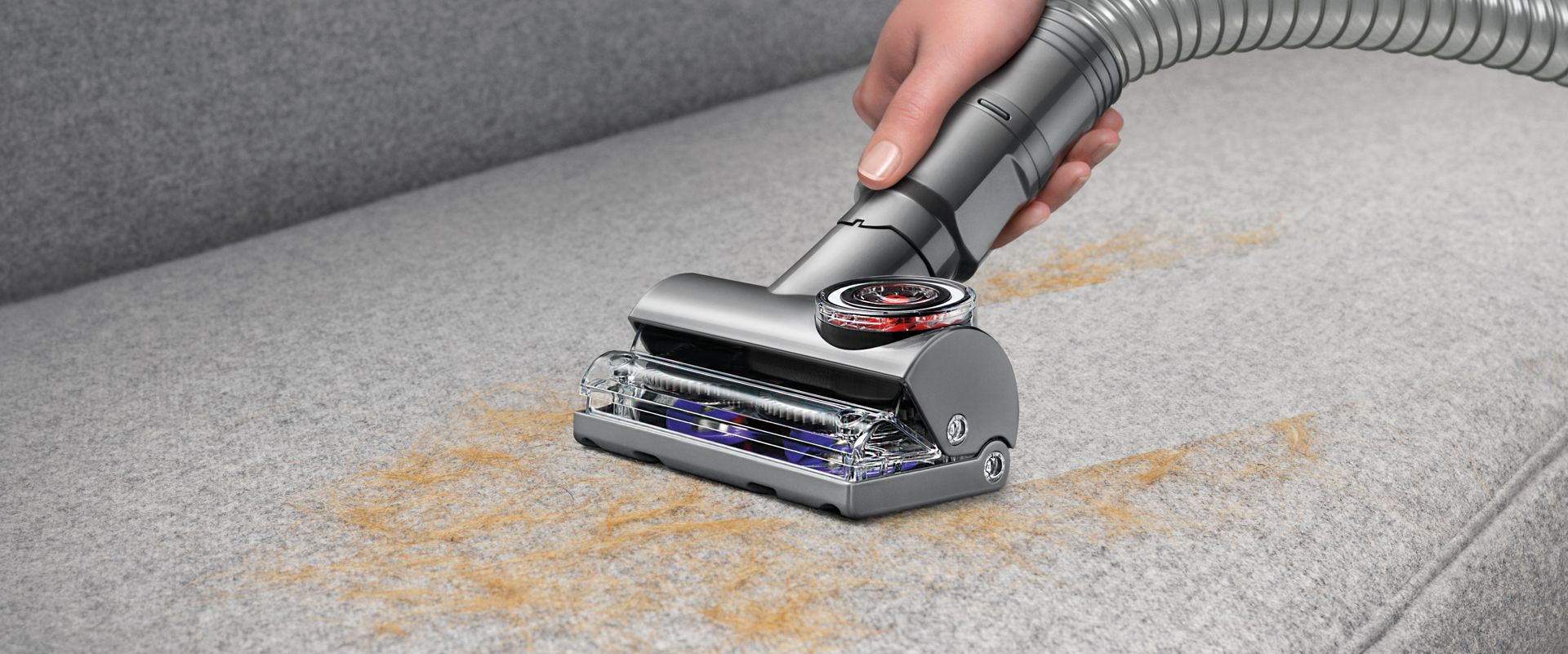 Close up of the Tangle-Free Turbine Tool being used to vacuum pet hair from a sofa