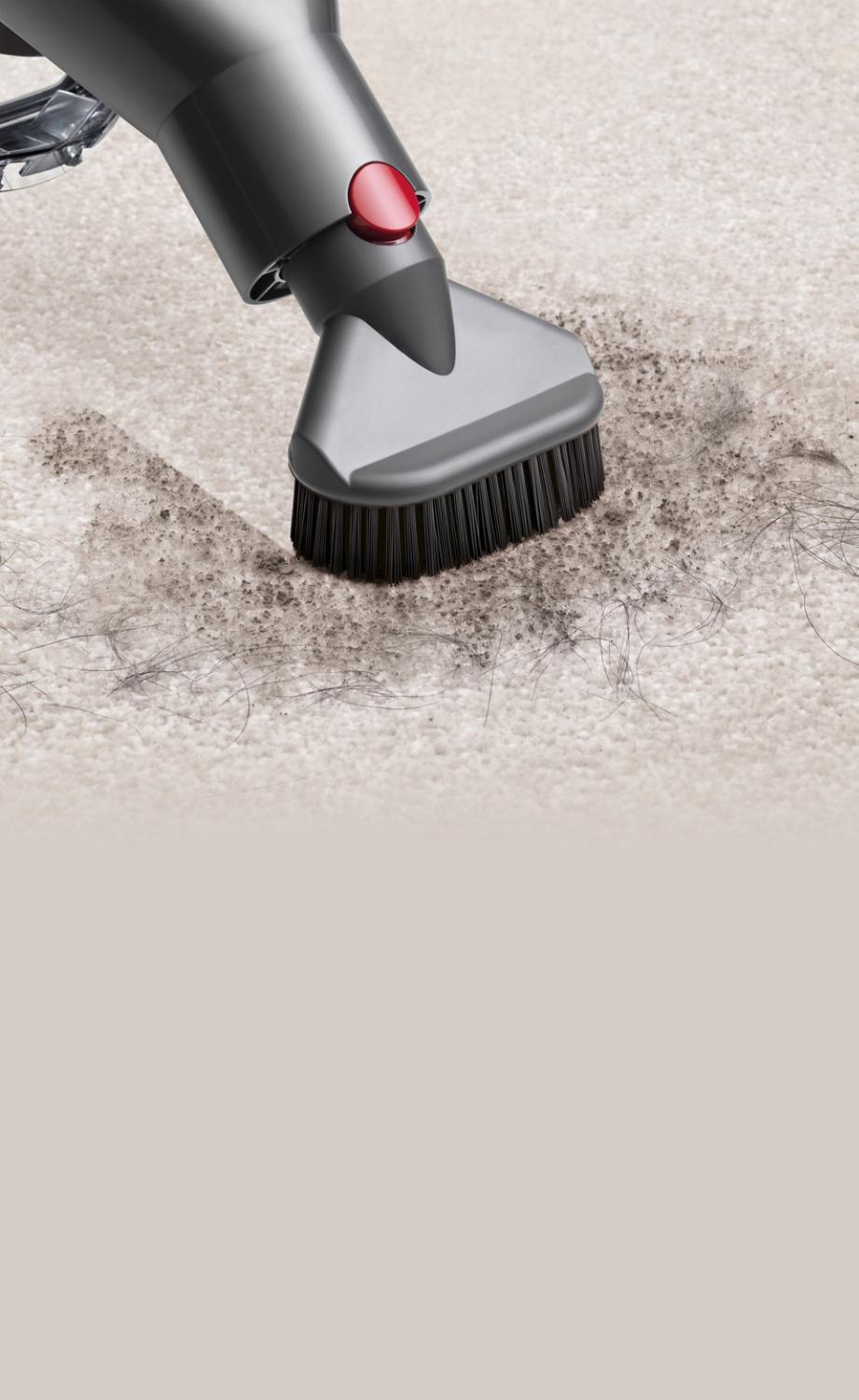 Close up of the Stubborn dirt brush tool being used to vacuum dirt and pet hair on a carpet