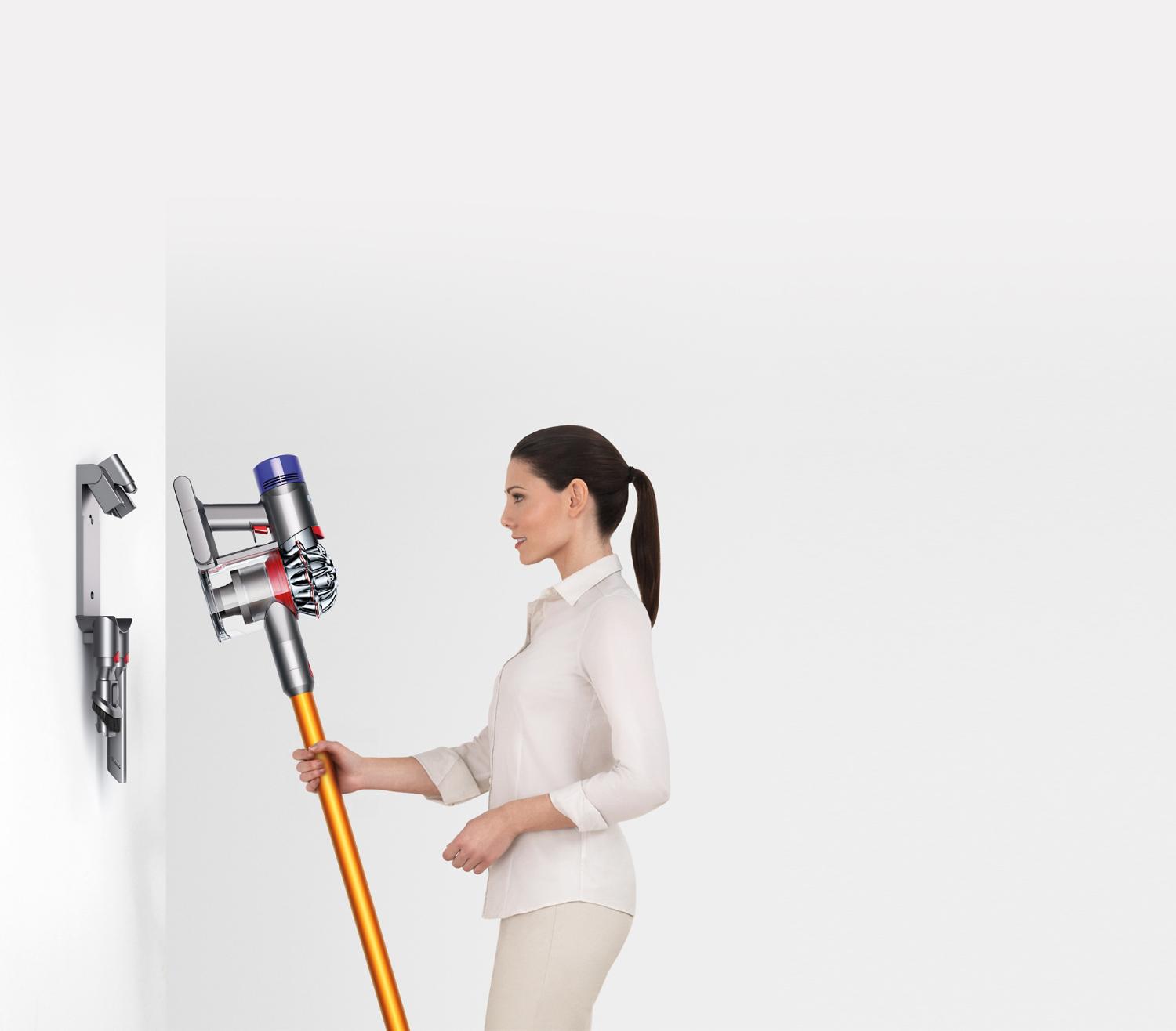 Femme insérant l’aspirateur balai Dyson dans la station d’accueil au sol pour le V7 et le V8.
