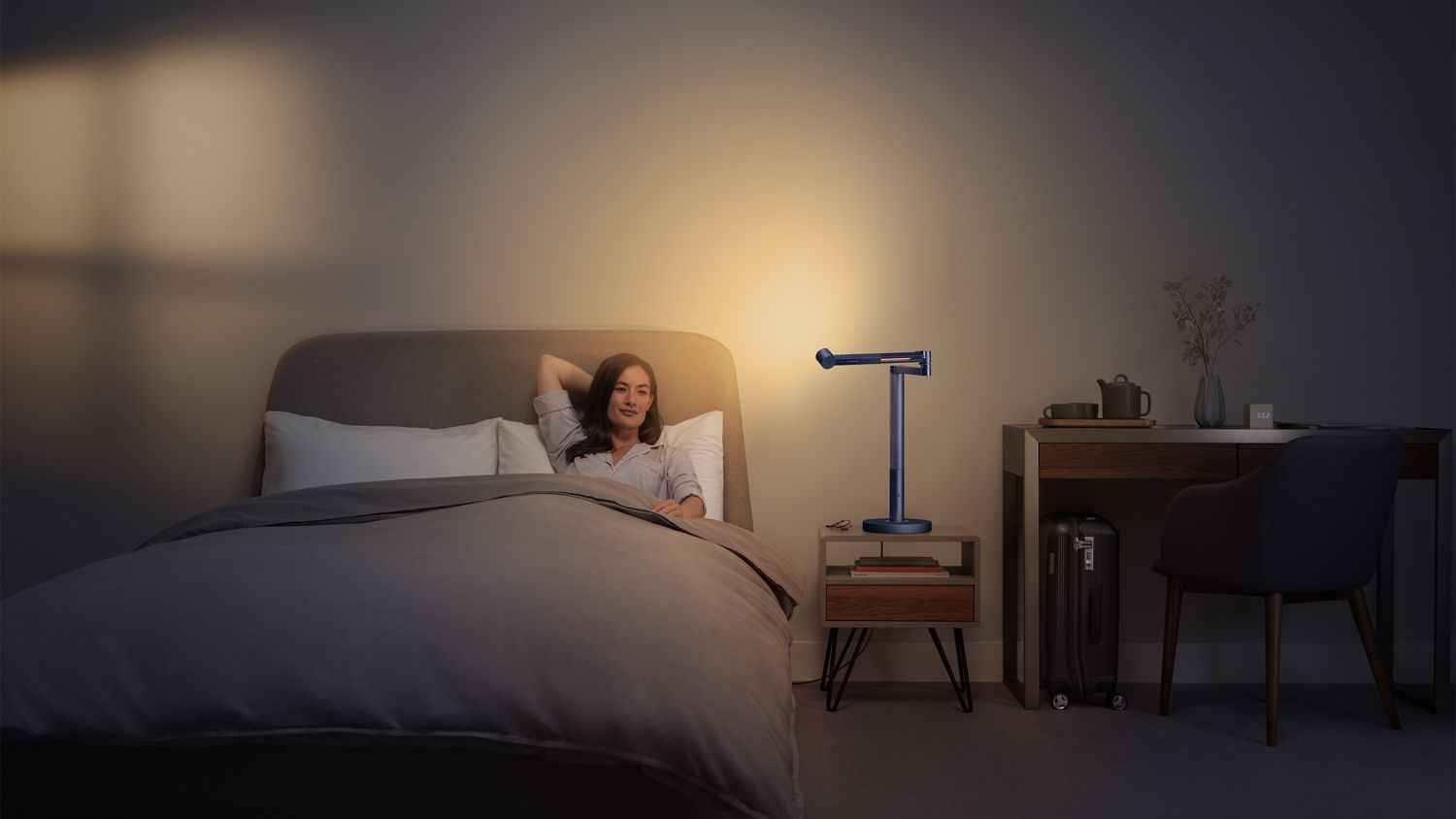 Une femme se détend sur un canapé, la lampe Dyson Solarcycle Morph éclairant le mur au-dessus d'elle et créant une lumière d'ambiance dans la pièce.