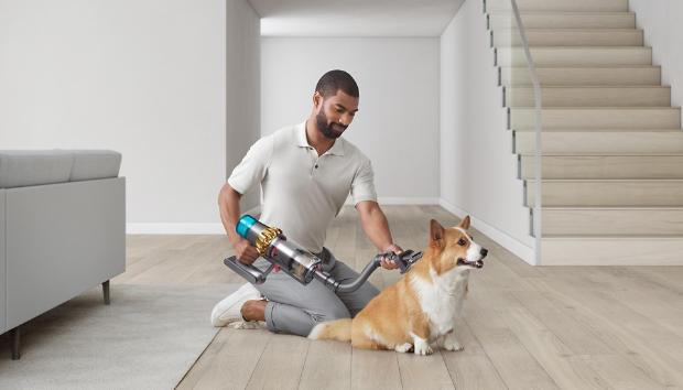 Mężczyzna używający końcówkę do groomingu zwierząt z odkurzaczem bezprzewodowym Dyson na swoim psie