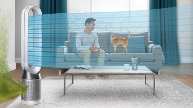 Mężczyzna siedzący na kanapie z kotem, podczas gdy oczyszczacz powietrza Dyson oczyszcza powietrze w domu