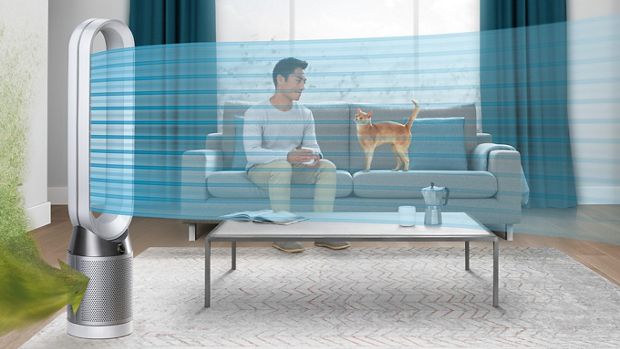 Mężczyzna siedzący na kanapie z kotem, podczas gdy oczyszczacz powietrza Dyson oczyszcza powietrze w domu
