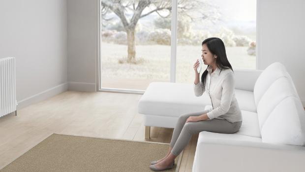 Kobieta siedząca na kanapie w salonie, kichająca w chusteczkę